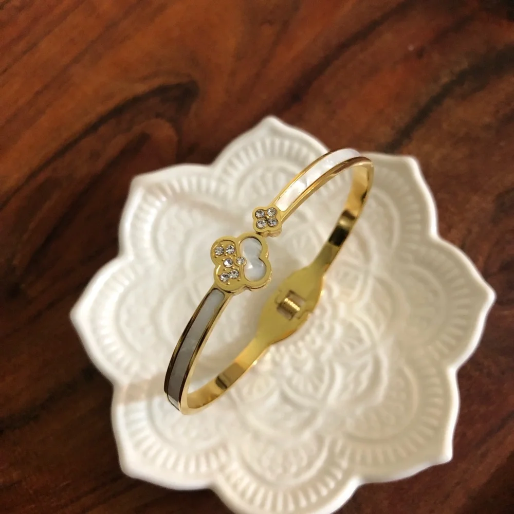 gold-toned hinged bangle bracelet featuring white clover motifs and crystal New